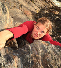A view directly above a young woman climbing a rock face. She is determined to succeed.