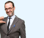 Teacher man using glasses proud, excited and arrogant, pointing with victory face isolated over blue background